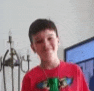 a young boy wearing a red shirt is standing in front of a television in a living room .