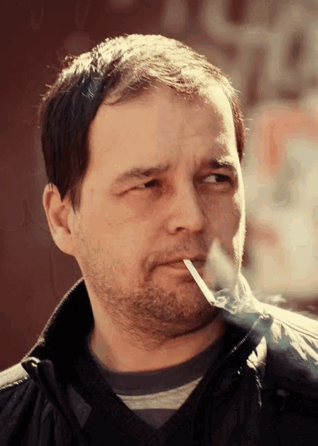 a man with a beard is smoking a cigarette and looking at the camera