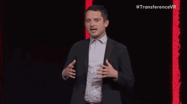 a man with a beard is wearing a suit and tie and speaking into a microphone .