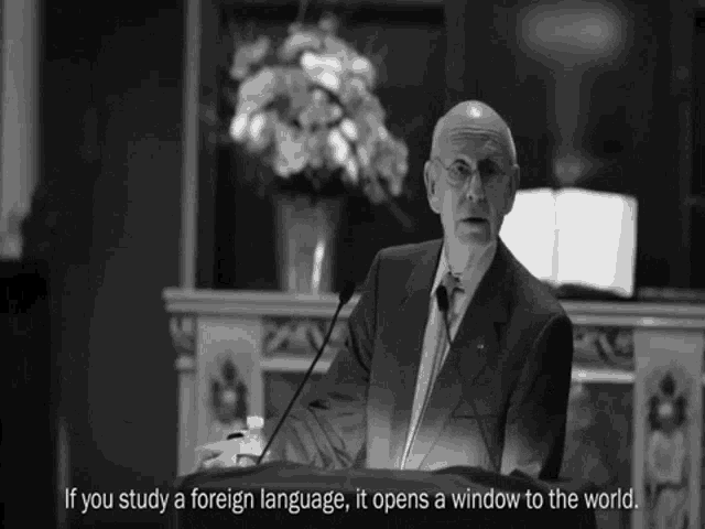a man stands at a podium with the words if you study a foreign language it opens a window to the world written below him