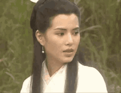 a woman with long black hair and earrings is wearing a white robe and looking at the camera .