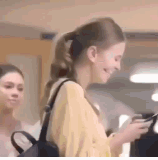 a woman is smiling and looking at her phone while another woman looks on .