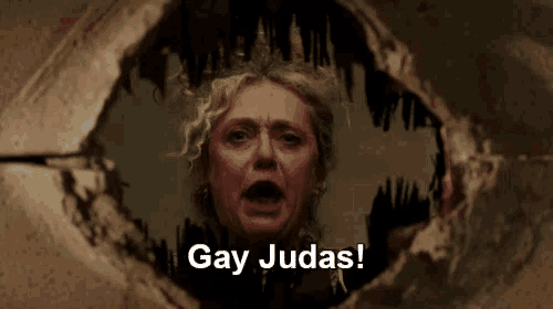 a woman is looking through a hole in a wall with the words `` gay judas '' written above her .