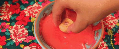 a person is dipping a donut in red frosting in a bowl .