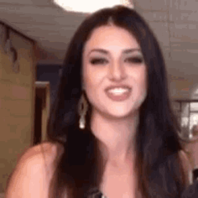a woman with long dark hair is smiling for the camera in a hallway .
