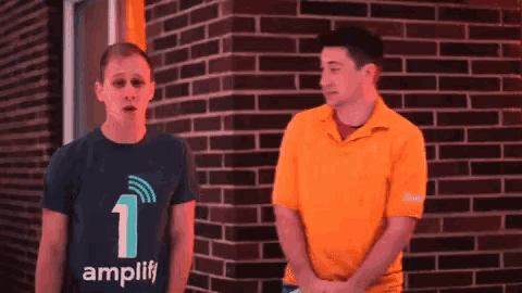 two men are standing in front of a brick wall and one has a shirt that says amplify
