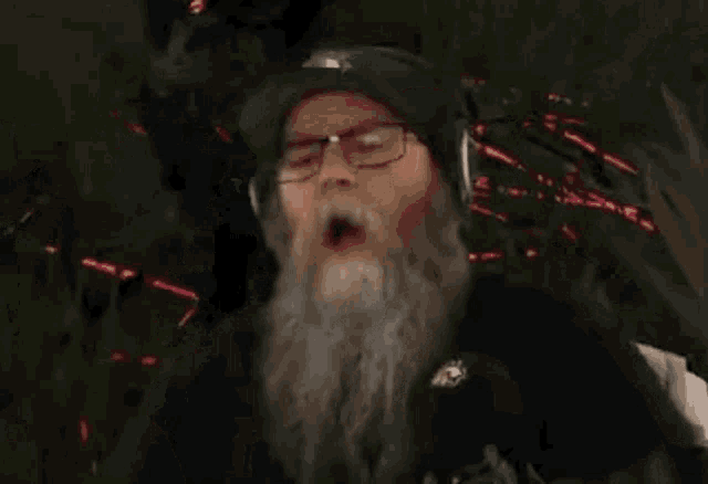 a man with a beard and glasses is holding a gun in his hand and making a fist .