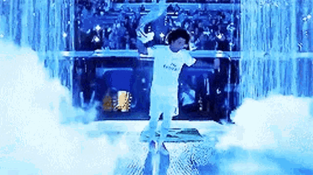 a man in a white shirt is standing in front of a blue waterfall .