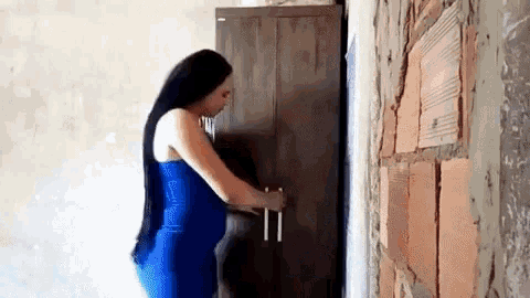 a woman in a blue dress is opening a wooden cabinet