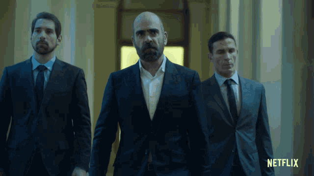 three men in suits and ties are walking down a hallway with a netflix logo behind them