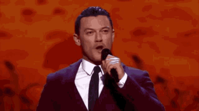 a man in a purple suit and tie is singing into a microphone on a stage .