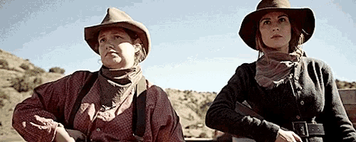 two women wearing cowboy hats and scarves are standing next to each other holding guns .
