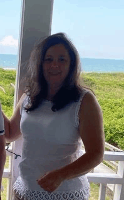 a woman in a white tank top and white shorts is standing on a balcony overlooking the ocean .