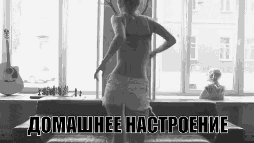 a woman in a bra and shorts is dancing in front of a window in a black and white photo .