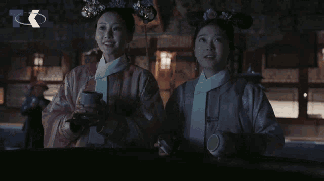 two women standing next to each other in a dark room with a t on the bottom right