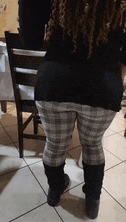 a woman wearing plaid pants and black boots is standing on a tile floor .