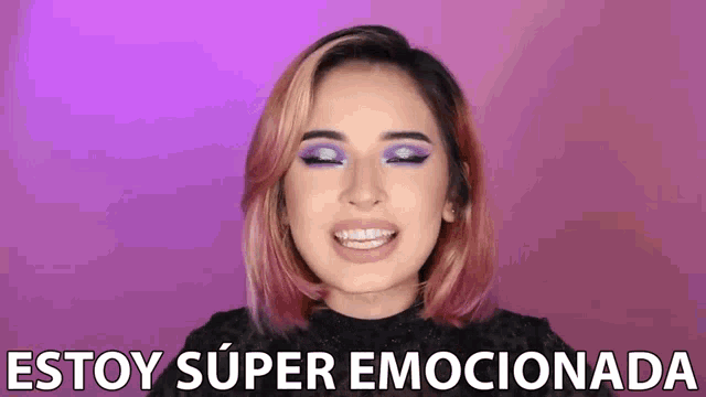 a woman with pink hair and purple eyeshadow is smiling and says estoy super emocionada .