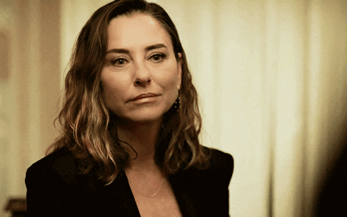 a woman wearing a black jacket and earrings looks at the camera