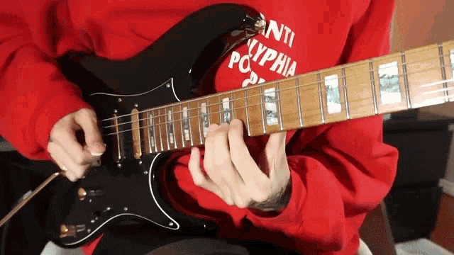 a person in a red sweatshirt playing a black guitar