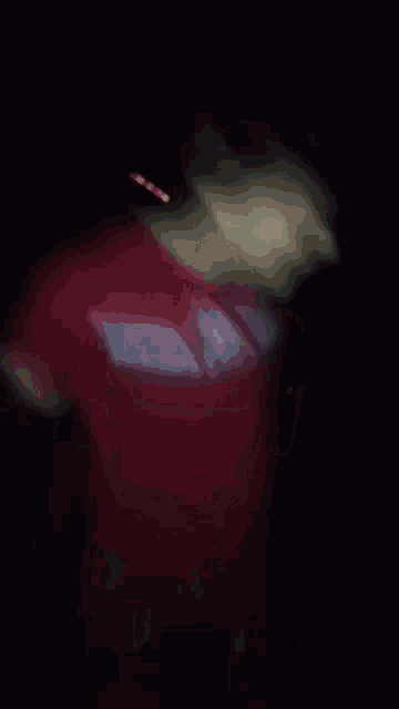 a blurry picture of a man in a red shirt making a funny face in the dark .