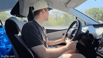 a man in a hat is driving a car with imgflip.com at the bottom