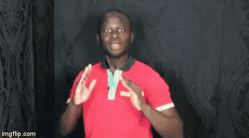 a man in a red shirt is standing in front of a black wall and making a funny face .