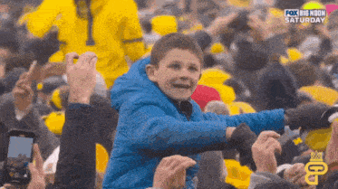 a boy in a blue jacket stands in a crowd with fox big noon saturday written on the bottom