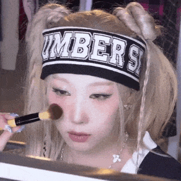 a woman wearing a headband with the word umbers on it is applying makeup with a brush .