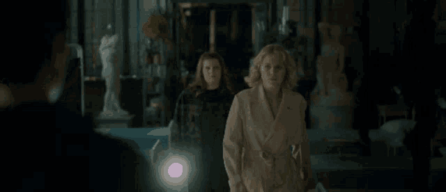 two women are walking in a dark room with a man holding a light .