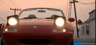 a red car with the headlights on is parked on the street