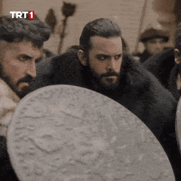a man in a fur coat holds a shield in front of a sign that says trt1