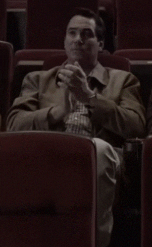a man in a brown jacket is sitting in a theater