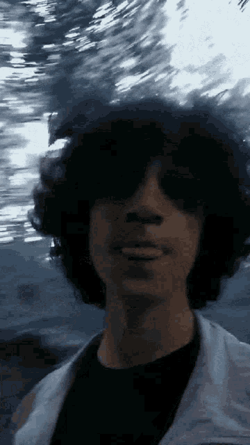 a young man with curly hair and sunglasses looks at the camera