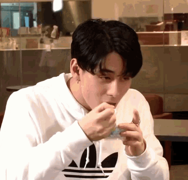 a man wearing a white adidas hoodie is eating something