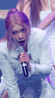a woman with pink hair is kneeling down holding a microphone