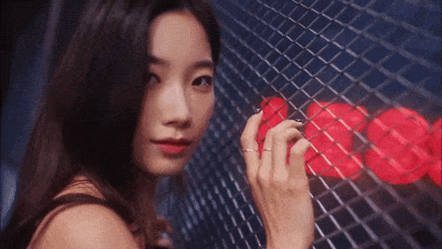 a woman behind a chain link fence with a red heart on the wall behind her