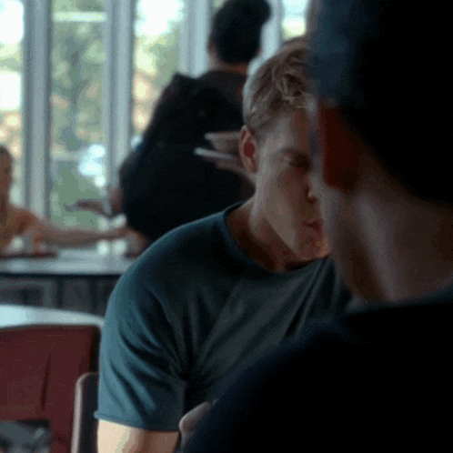 a man in a green shirt is sitting at a table talking to another man