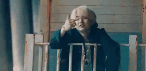 a young man is standing on a balcony making a peace sign with his finger .