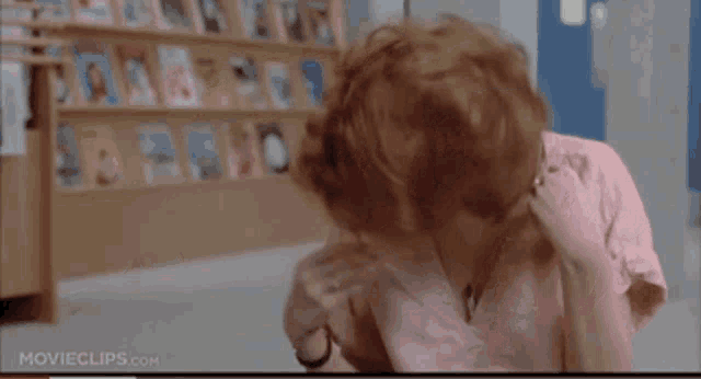a woman in a pink shirt is sitting in front of a book shelf ..