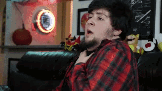 a man in a red and black plaid shirt is sitting on a couch in front of a pepsi sign