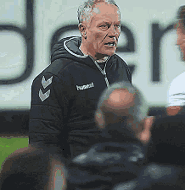 a man wearing a hummel jacket stands in front of a group of people