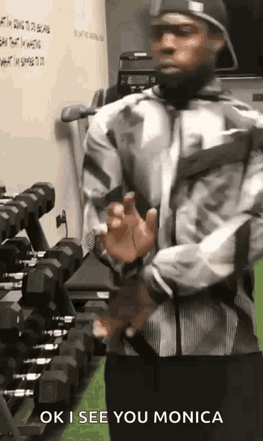 a man is standing in front of a row of dumbbells in a gym and says ok i see you monica .