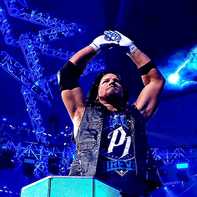 a wrestler wearing a black vest with the letter p on it raises his hands in the air