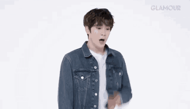 a young man wearing a denim jacket is standing in front of a white background .
