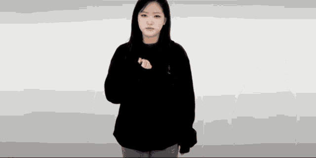a woman in a black hoodie is standing in front of a white background and making a funny face .