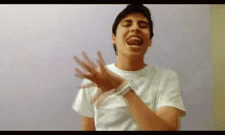 a young man in a white t-shirt is making a funny face with his mouth open .