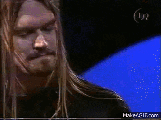 a man with long blonde hair and a beard is playing a guitar in front of a blue background .