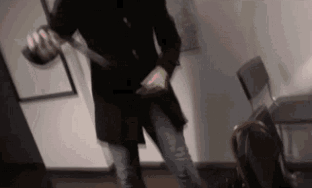 a man in a black coat is holding a large knife in his hand .