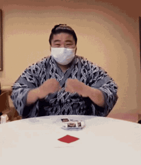 a man wearing a mask is sitting at a table with cards on it