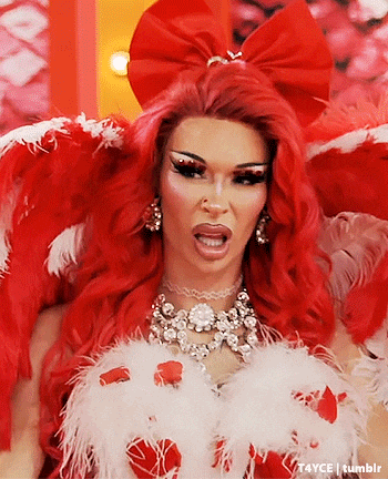 a drag queen with red hair and white feathers is wearing a red and white costume .